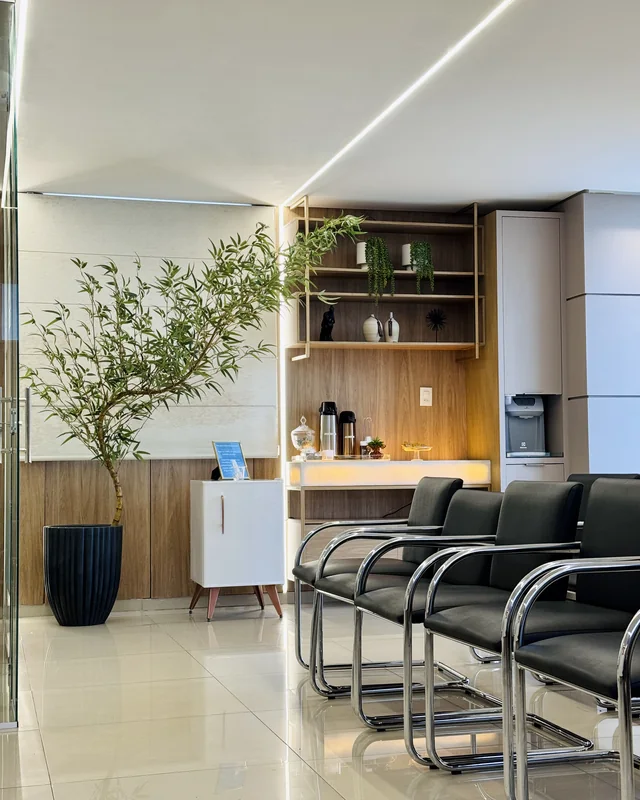 Sala de espera da ProVasc, com poltronas, oliveira e estação de café